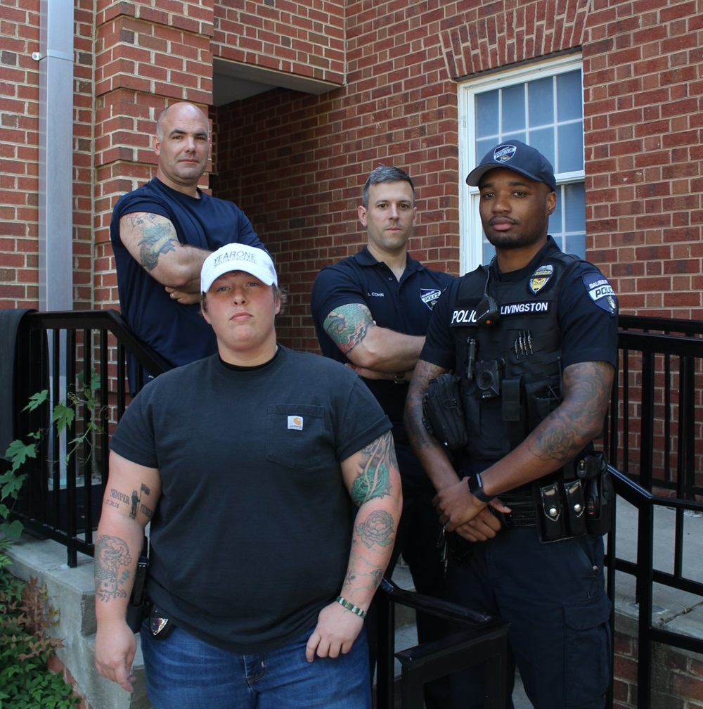 Four officers posed in front of police headquartes, with the uniform sleeves rolled up to show their arm tattoos.